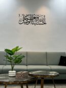 Modern Arabic calligraphy wall art in matte black acrylic displaying "Hasbunallahu Wa Ni’mal Wakeel" above a stylish sofa in a contemporary living room.